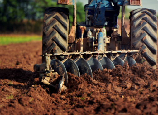 A tractor plows a field with a disc harrow, turning over soil under a clear sky