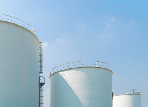 Large white cylindrical storage tanks with metal railings under a clear blue sky